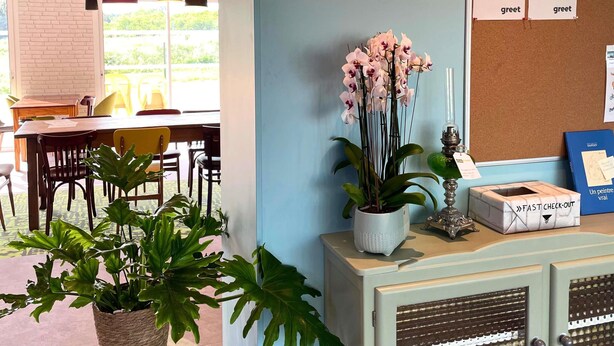 Un espace d’accueil avec une pancarte « Bienvenue », une plante en pot, une pancarte « DÉPART RAPIDE » et un panneau d’affichage où sont accrochées des petites notes de bienvenue.