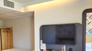 A hotel room with a bed, a small table with a magazine, a mounted TV, and a mirror with a wooden frame. - greet hotel Castets Coeur des Landes (Castets)