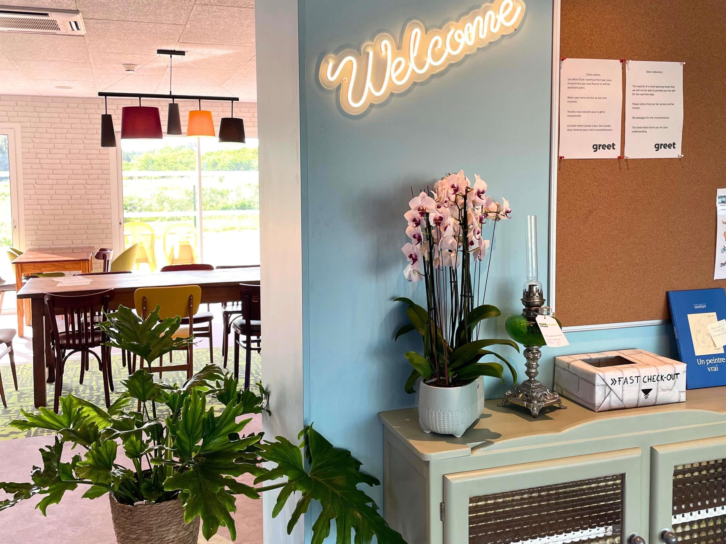 Un espace d’accueil avec une pancarte « Bienvenue », un tableau d’affichage où sont affichées des notes de bienvenue, une plante et une pancarte « DÉPART RAPIDE ».