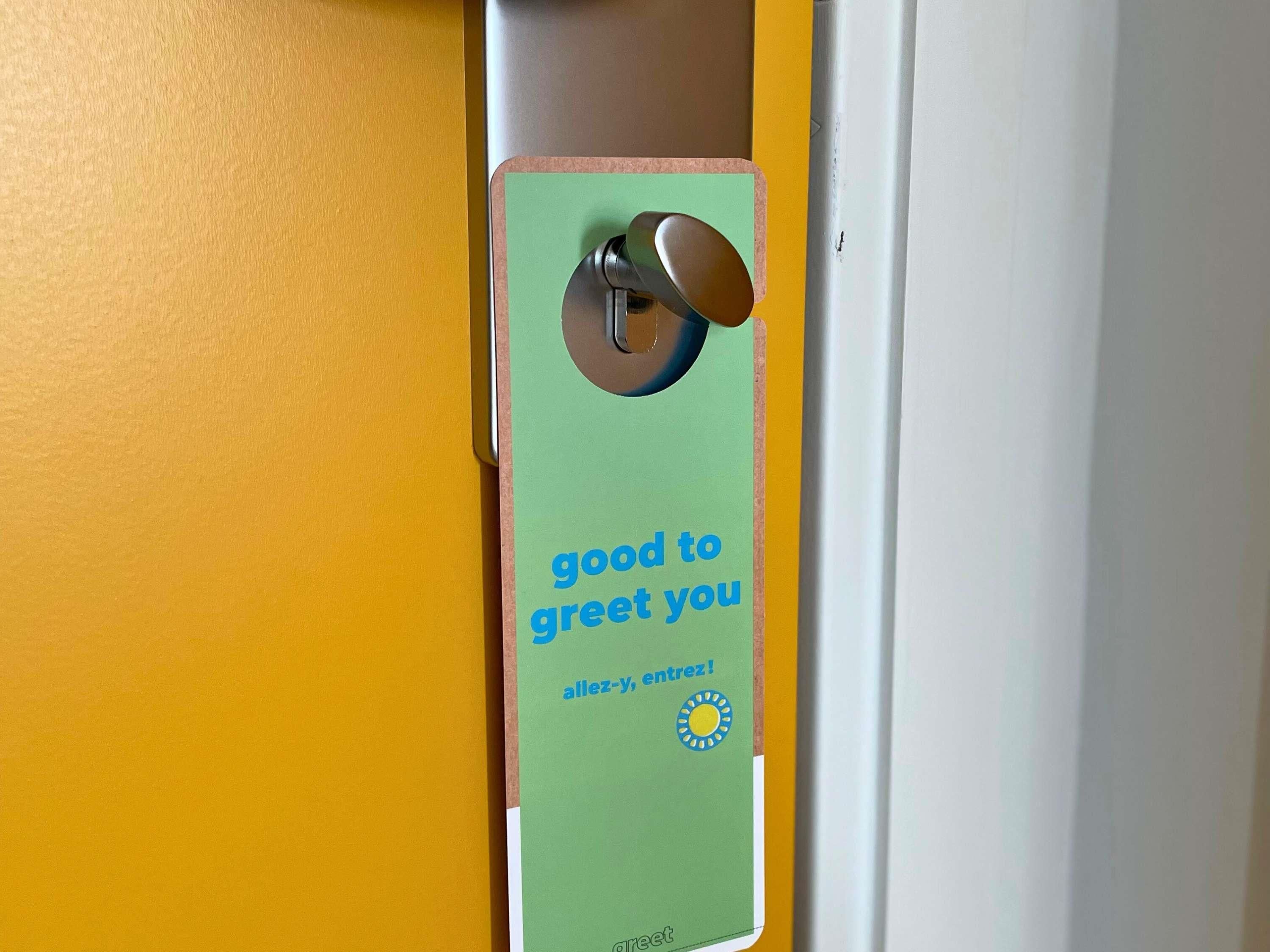 A door with a green card hanger that reads 'good to greet you' and 'allez-Y entrez!'