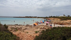 Une plage au paysage rocheux, où l’on voit des gens nager et bronzer, et un bâtiment blanc en arrière-plan.