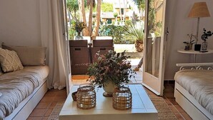 Une pièce comprenant deux canapés, une table basse agrémentée d’objets décoratifs et donnant sur un jardin planté de palmiers.