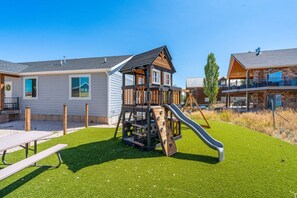 A playground with a slide and climbing structure, surrounded by houses with a well-maintained lawn.