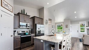 A spacious kitchen with granite countertops, stainless steel appliances, and a central island with bar stools. - Bear Lake Getaway |Sleeps 19, Hot Tub, Views, Ideal Beach, Ping-Pong! (Garden City)
