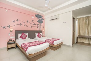 Una habitación de hotel con dos camas, un ventilador de techo, un equipo de aire acondicionado y un mural decorativo en la pared.