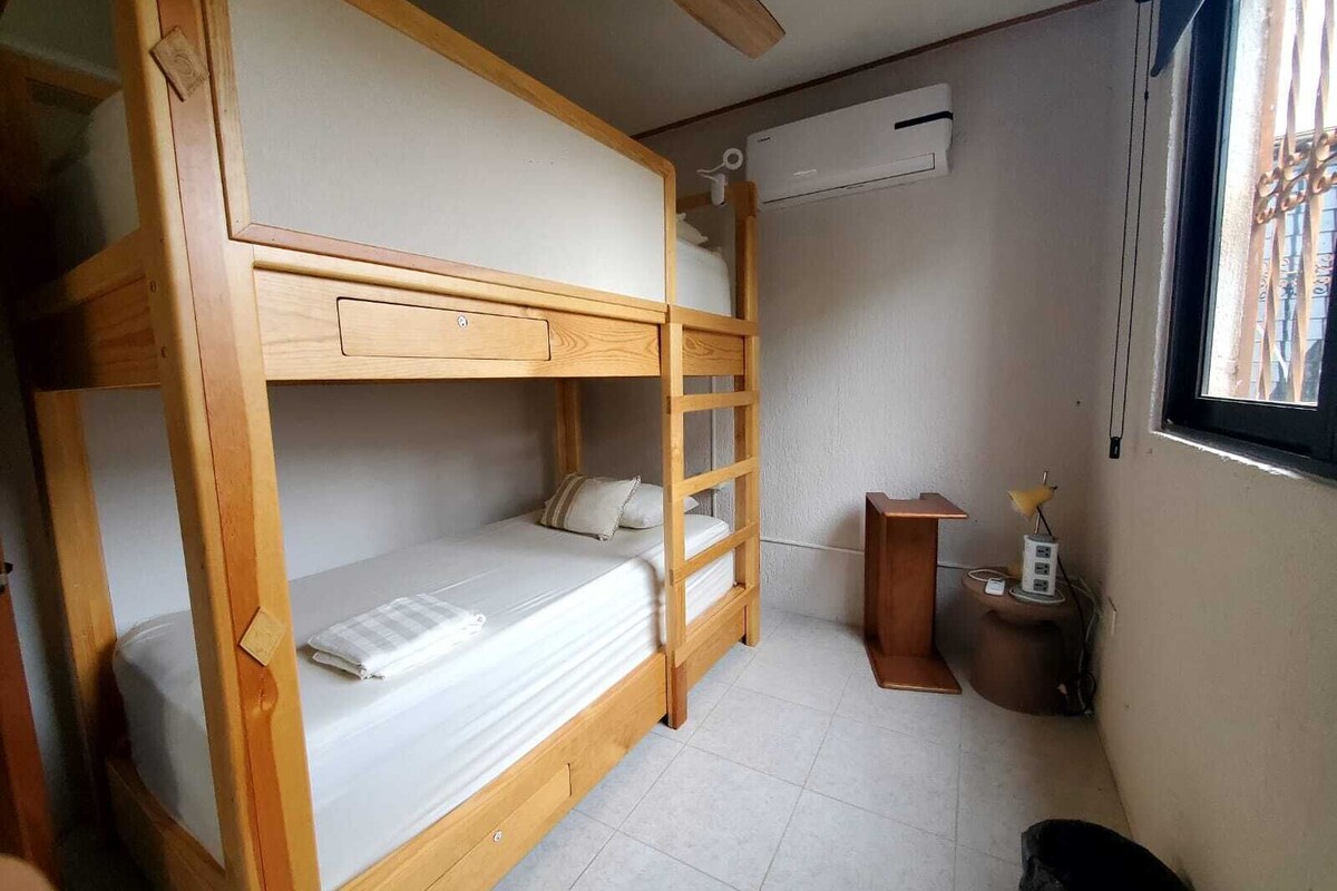 Une chambre avec un lit superposé, une échelle, une petite table avec une lampe et un appareil de climatisation fixé au mur.