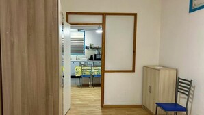 A room with a wooden floor, a blue chair, a cabinet, and a view into a kitchen area. - Azur apartment with sea view (Sainte-Anne)