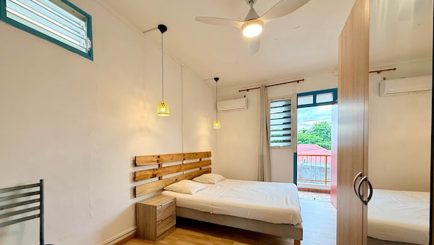 A bedroom with a bed, a chair, a desk, a wardrobe, a ceiling fan, and a window with blinds. - Azur apartment with sea view (Sainte-Anne)