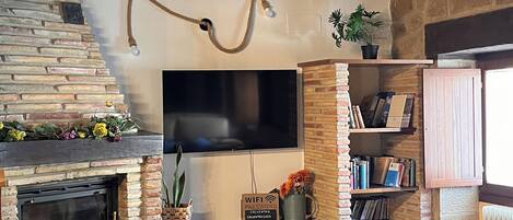 A cozy living room with a fireplace, a flat-screen TV mounted on the wall, and a bookshelf filled with books.