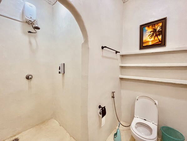 Une salle de bain équipée d’un WC, d’une douche, d’un porte-serviettes, d’un distributeur de savon et d’un tableau accroché au mur.