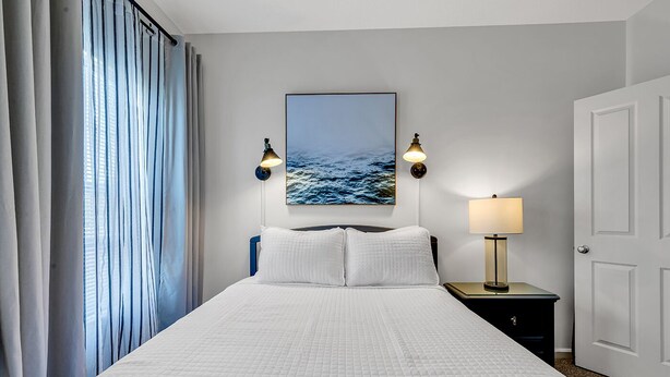 A hotel room with a large bed, two wall-mounted lamps, a nightstand, a door, and a window with curtains. - Legends Golf Condo Steps From Ailsa Pub & Pool (Myrtle Beach)