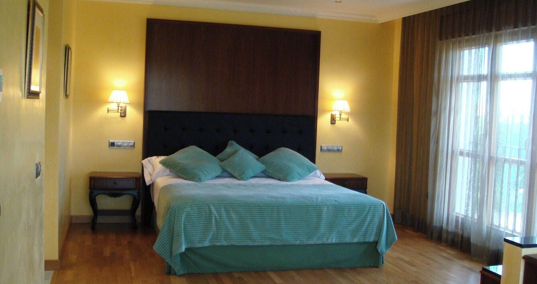 Una habitación de hotel con una cama grande, dos mesitas de noche, un cabecero oscuro y dos lámparas fijadas a la pared.
