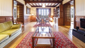 Un salón comedor amplio con techo de madera, una mesa de centro de vidrio, un sofá, una mesa de comedor con sillas y una estantería.