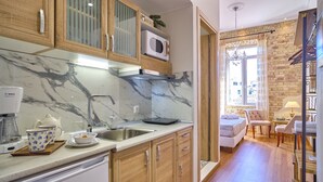 Een keuken met marmeren aanrechtbladen, houten kastjes en een magnetron. Er is een spoelbak, een koffiezetapparaat en een theeservies. De kamer heeft een bakstenen muur en een raam met gordijnen.
