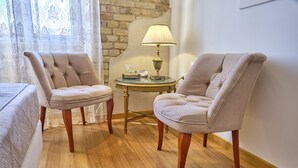 Een kamer met twee beige fauteuils, een klein rond tafeltje met een lamp en een bed met een witte dekbedovertrek.