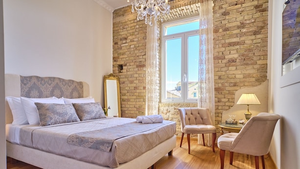 Een slaapkamer met een groot bed, een kroonluchter, een bakstenen muur en een raam met gordijnen.