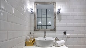 Een badkamer met witte metro tegels, een rond wastafel, een spiegel met een sierlijk lijstwerk en een handdoek op het aanrecht.