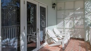 Ein überdachter Patio-Bereich mit weißen Stühlen, Fliesenboden und einer weißen Gitterwand.