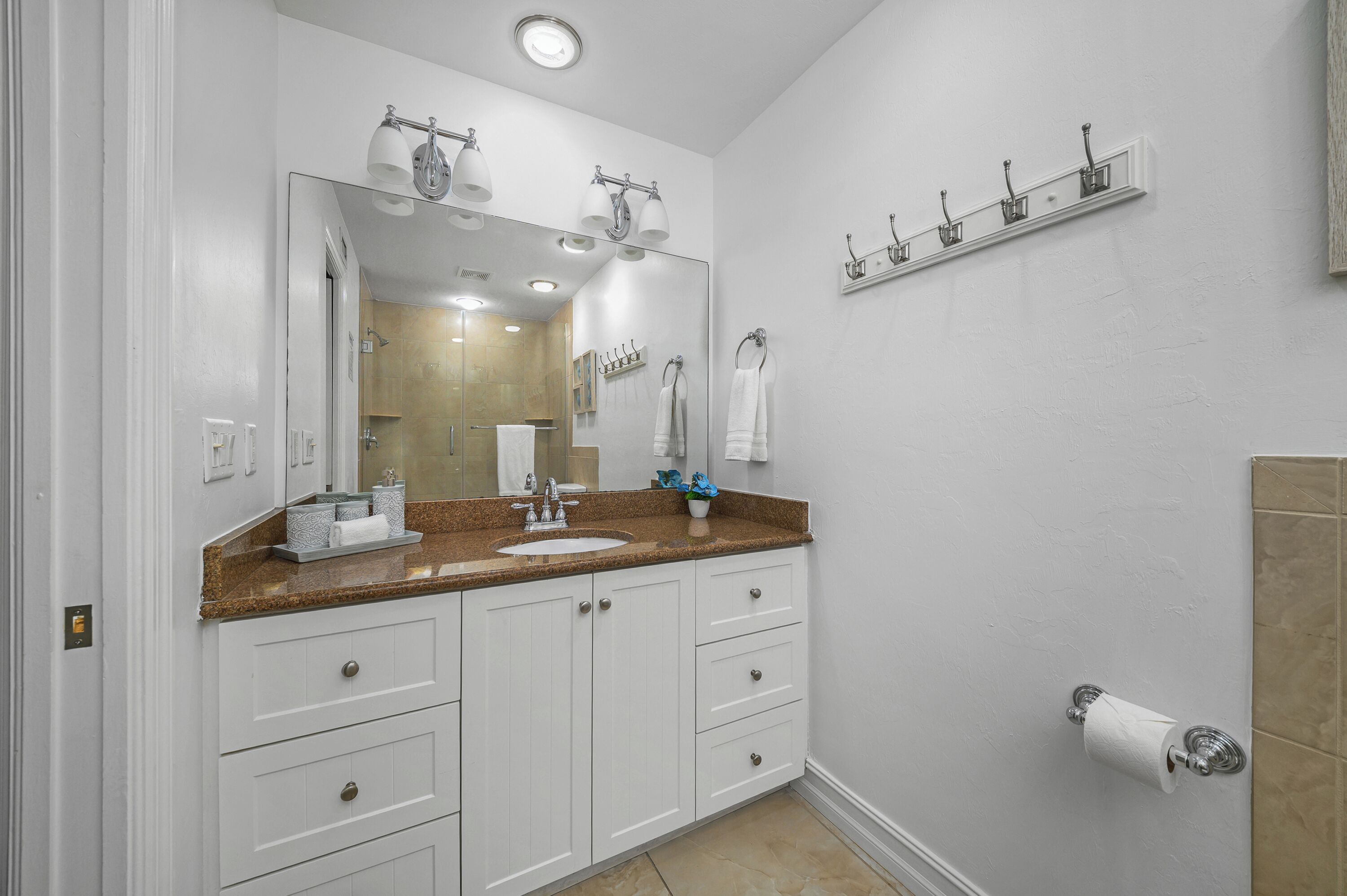 A bathroom with a large mirror, white cabinets, a sink, and a towel rack.
