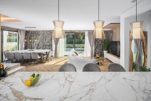 A modern dining area with a marble table, grey upholstered chairs, and pendant lighting.
