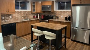 A modern kitchen with wooden cabinets, a stainless steel refrigerator, a microwave, and a coffee maker. - The Bachelor (Mirabel)