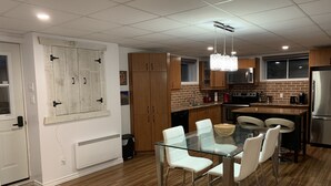 A modern kitchen with wooden cabinets, a glass dining table, and a stainless steel refrigerator. - The Bachelor (Mirabel)