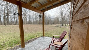 A covered patio with two red lounge chairs and a wooden table. - Country Cabin with Jacuzzi Tub and Meramec River Access and Pets welcome! (Bourbon)