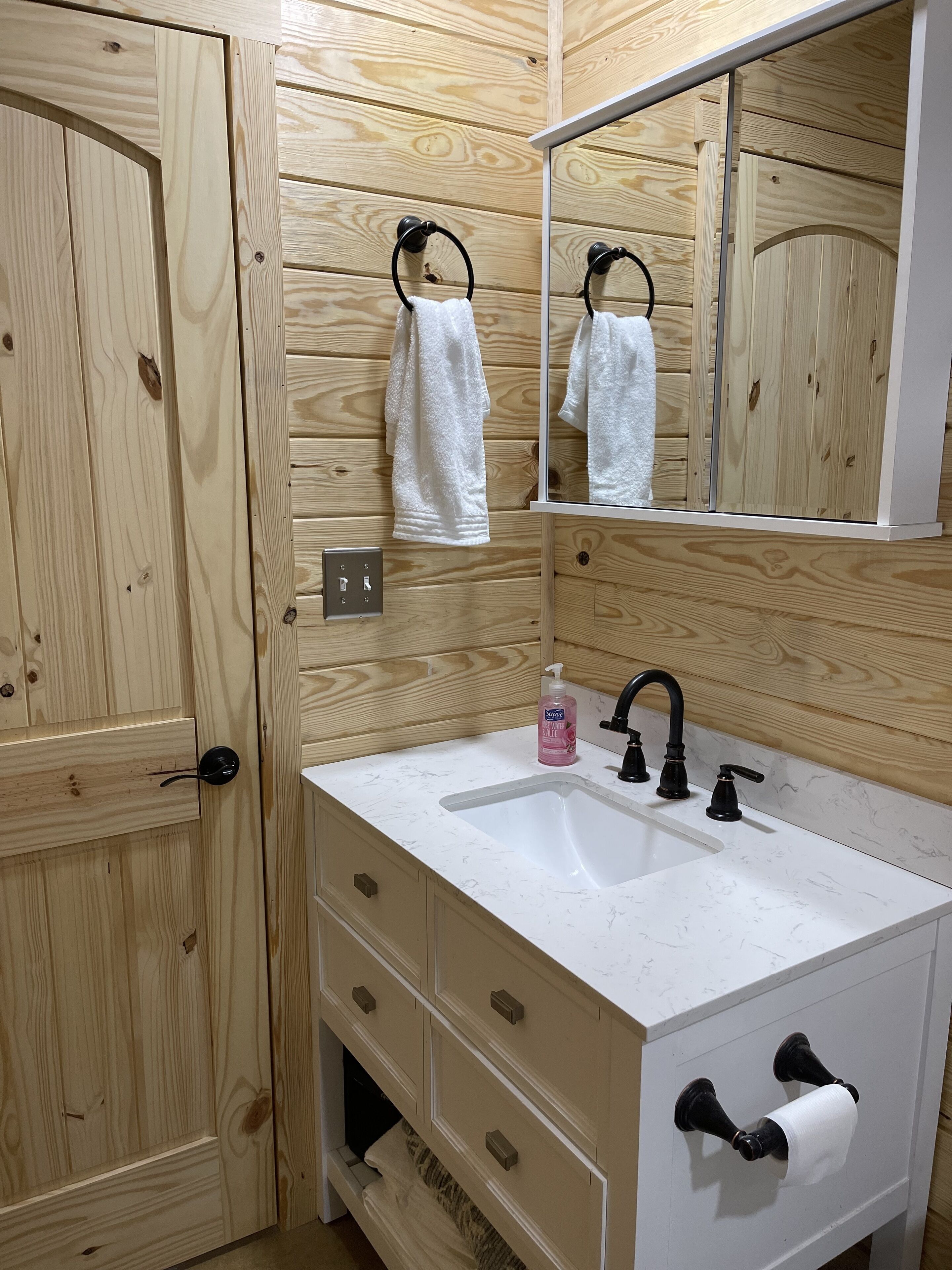 A bathroom with wooden panel walls, a white sink with a black faucet, a mirror, and a towel rack.