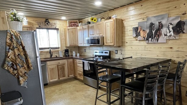 A kitchen with wooden cabinets, a refrigerator, a microwave, and a dining area with chairs. - Country Cabin with Jacuzzi Tub and Meramec River Access and Pets welcome! (Bourbon)