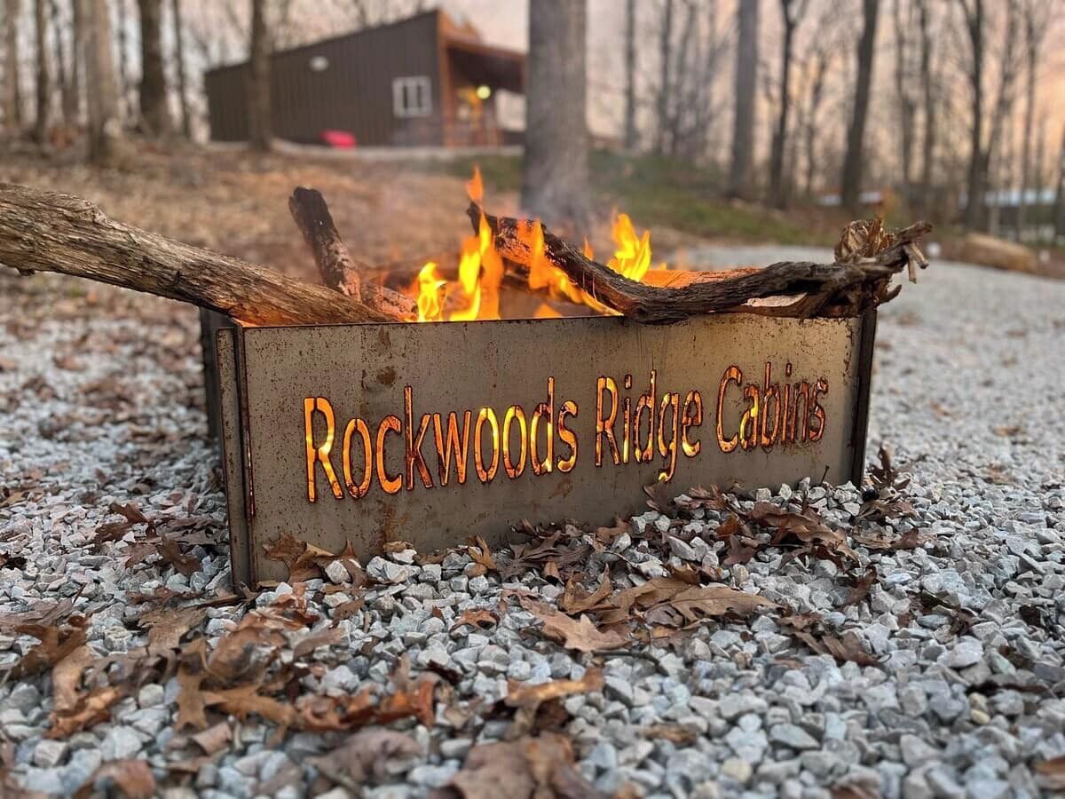 A metal fire pit with the text "Rockwoods Ridge Cabins" on it, surrounded by gravel and dry leaves.