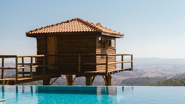 A wooden cabin with a tiled roof overlooking a clear blue pool. - Pousada do Xerife (Caconde)