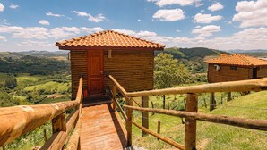A wooden cabin with a red door, a wooden staircase leading up to it, and a view of the surrounding landscape. - Pousada do Xerife (Caconde)