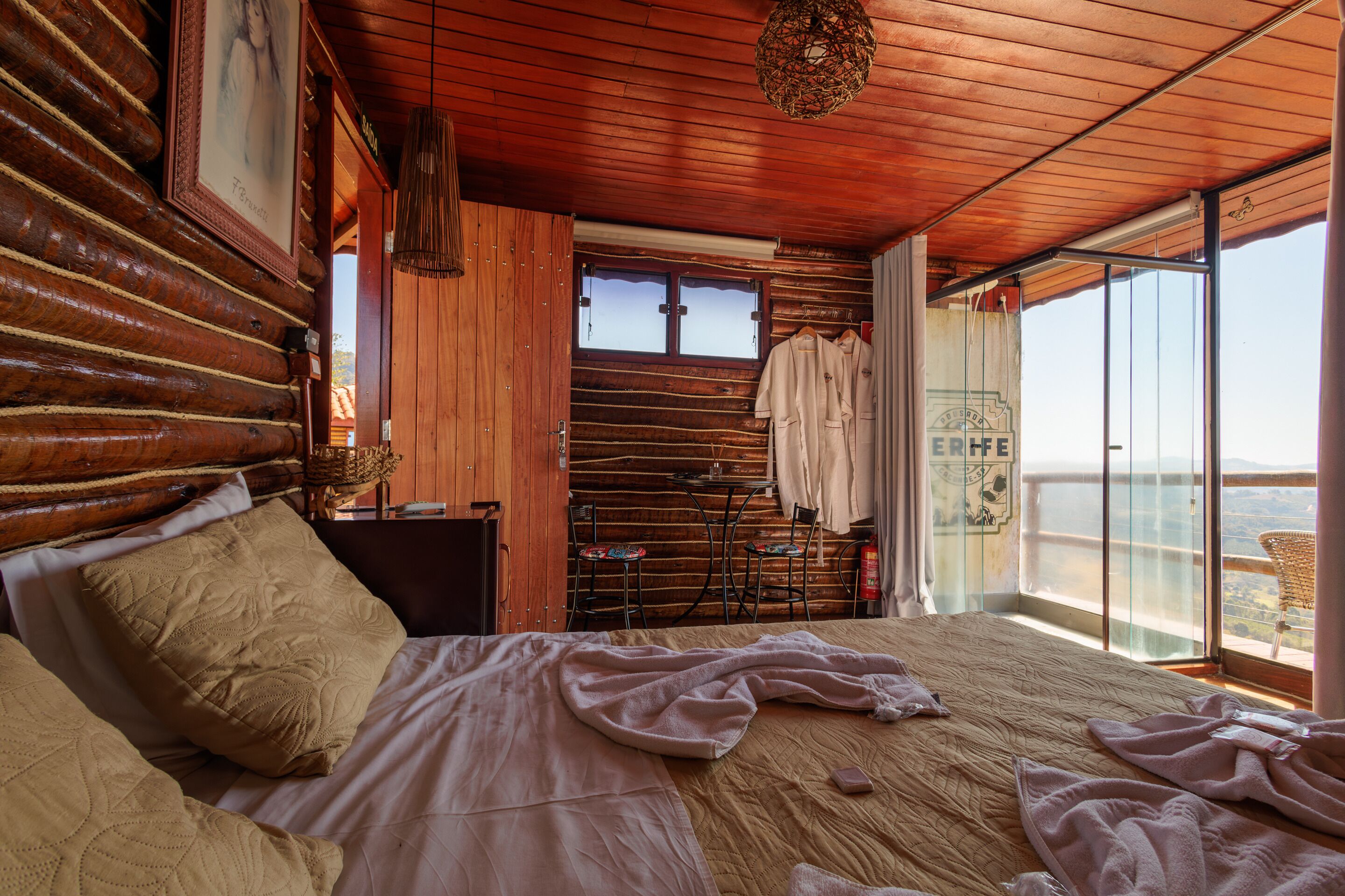 A log cabin-style bedroom with a large bed, wooden walls, and a balcony with a view.