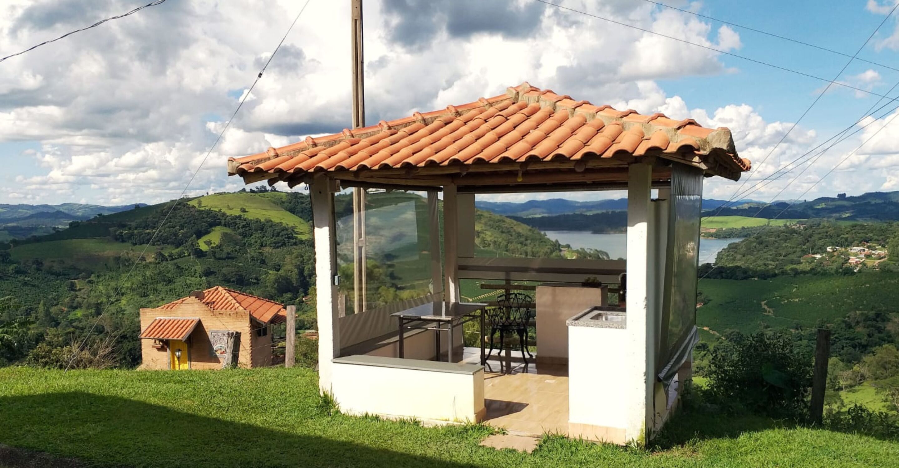 A small, rustic gazebo with a tiled roof overlooking a lush valley.