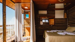 A log cabin bedroom with a large window, wooden walls, a bed, and a small table. - Pousada do Xerife (Caconde)
