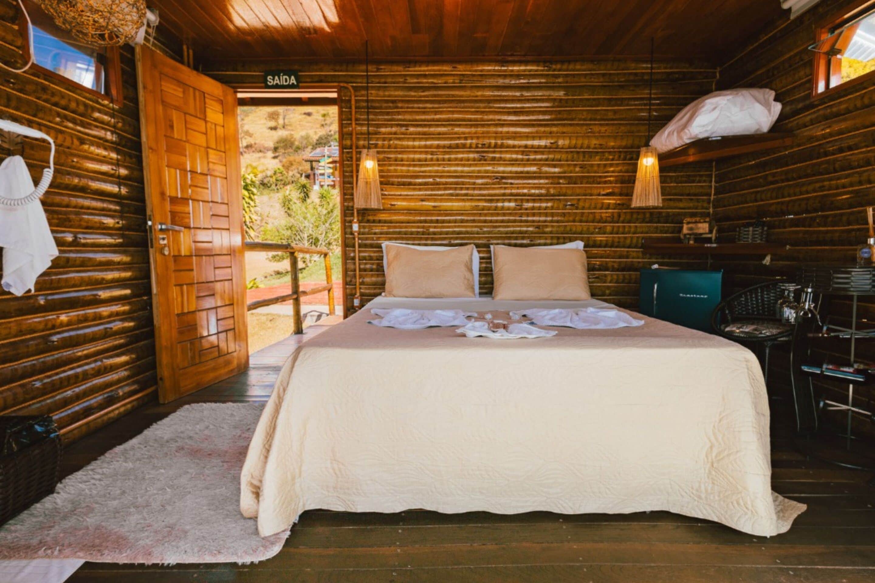 Acogedora habitación tipo cabaña de madera, con cama, una puerta que da al exterior y una pequeña mesa con sillas.