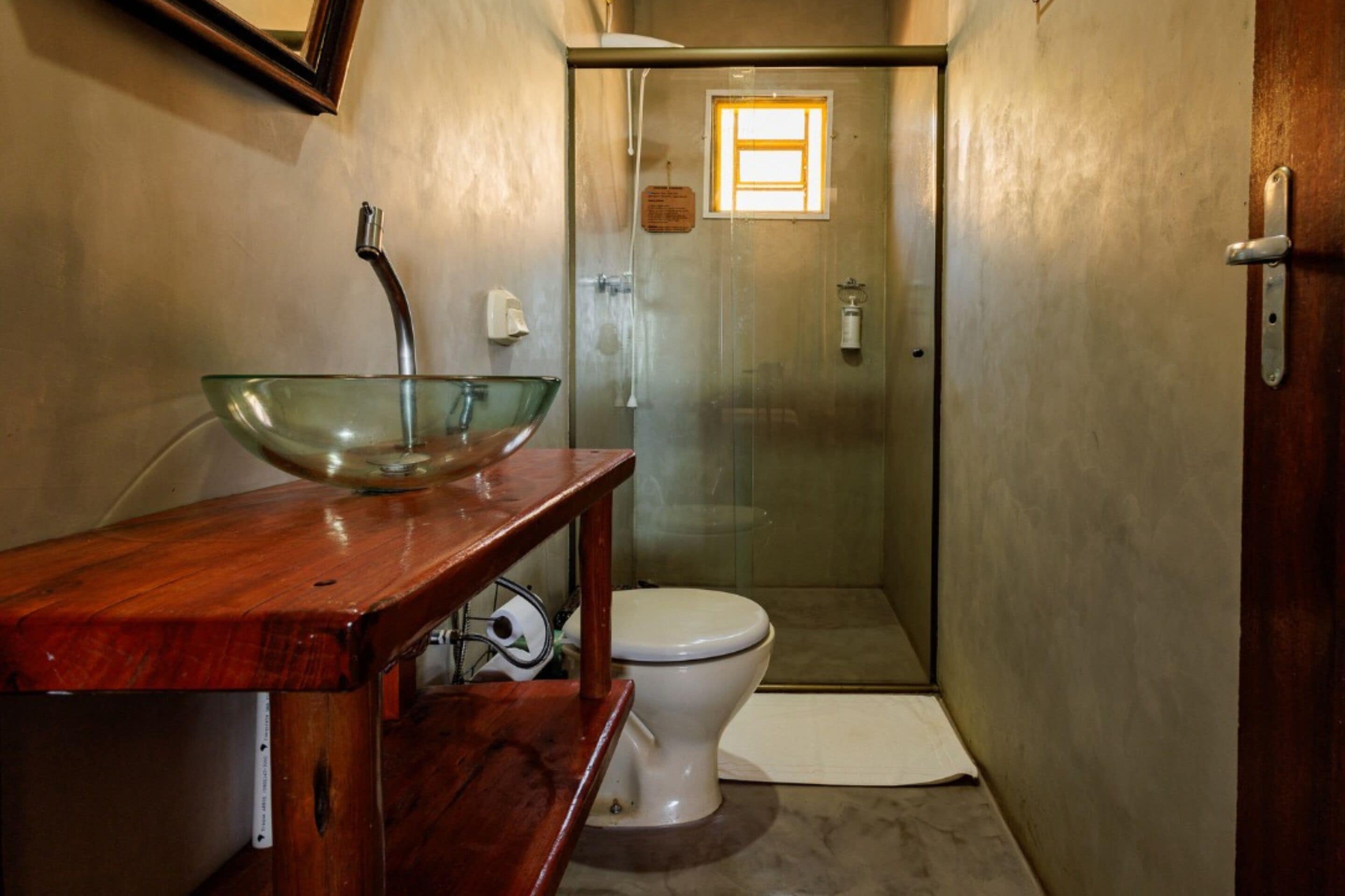 A bathroom with a glass bowl sink, a white toilet, and a glass-enclosed shower.