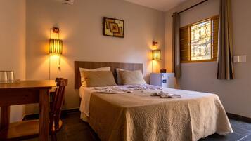 Quarto de hotel com cama, luminárias de cabeceira, escrivaninha e janela com cortinas.