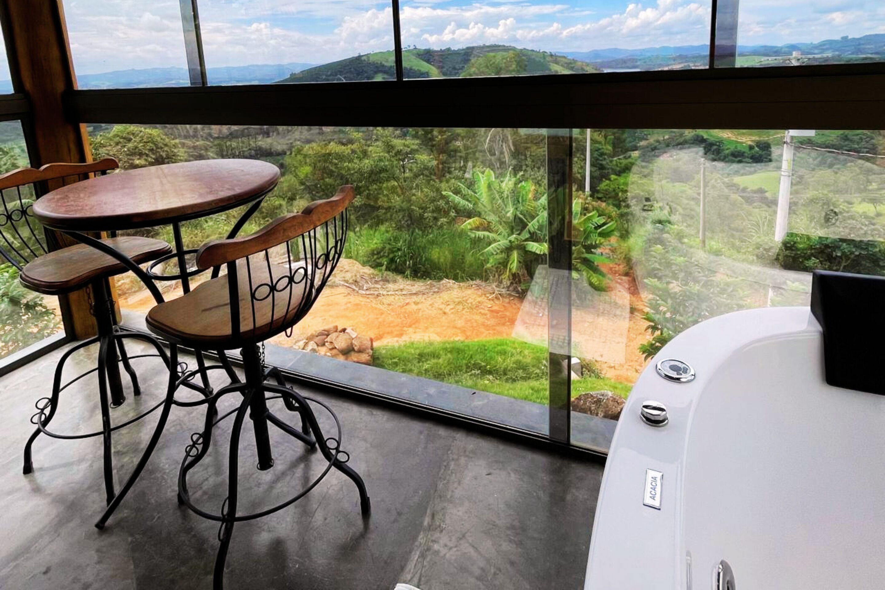 Un balcon avec une table et des chaises, une vue sur un paysage vallonné et une baignoire blanche.