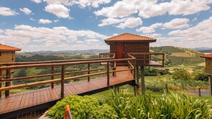 A wooden deck with a wooden railing overlooking a lush valley. - Pousada do Xerife (Caconde)