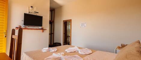 Une chambre d’hôtel avec un lit, un téléviseur posé sur un meuble, un ventilateur de plafond et une petite table.