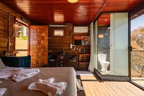 Una habitación de cabaña de madera con una cama, una mesa y una silla. Hay una ventana con vistas a árboles.
