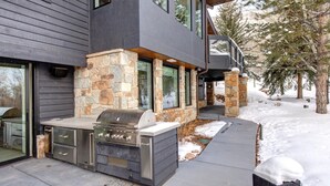 Una casa moderna con fachada de piedra, ventanas amplias y una parrilla integrada al aire libre.