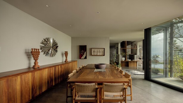 A spacious dining area with a long wooden table and wicker chairs, a decorative wall piece, and a view through large windows. - Ocean front house Punta de Mita (Punta de Mita)