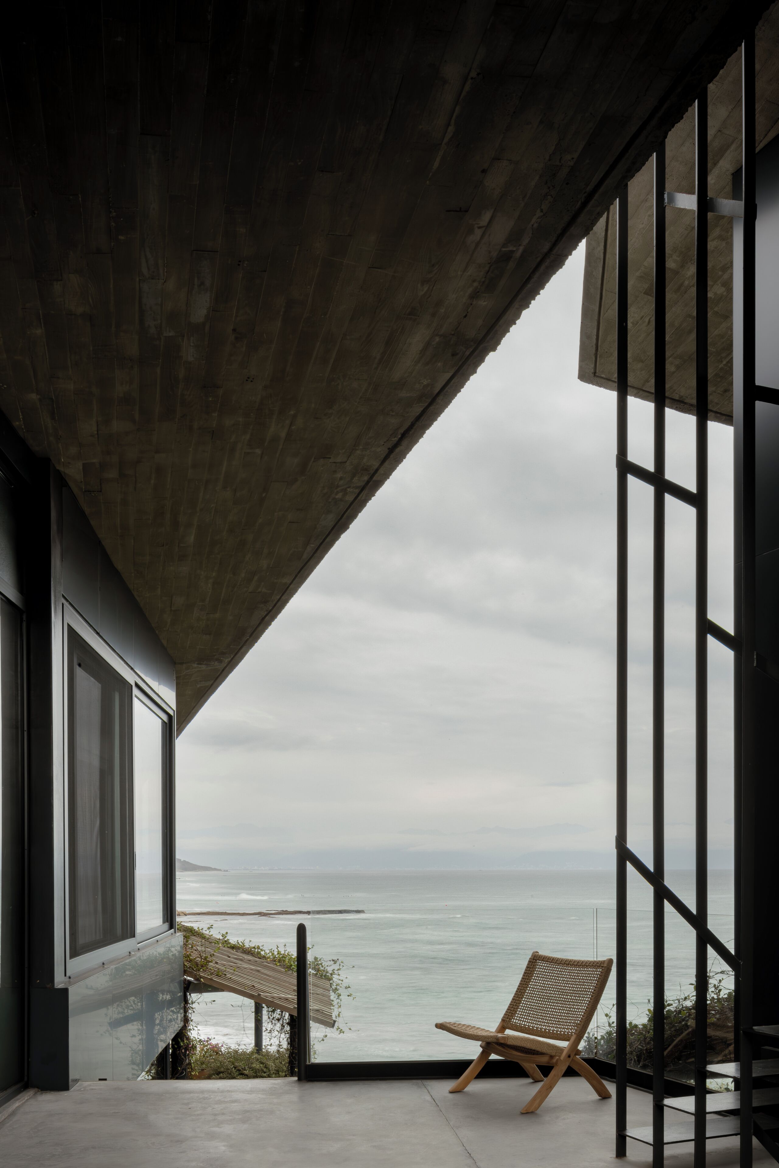 A modern interior with a concrete ceiling, large windows, and a view of the ocean.