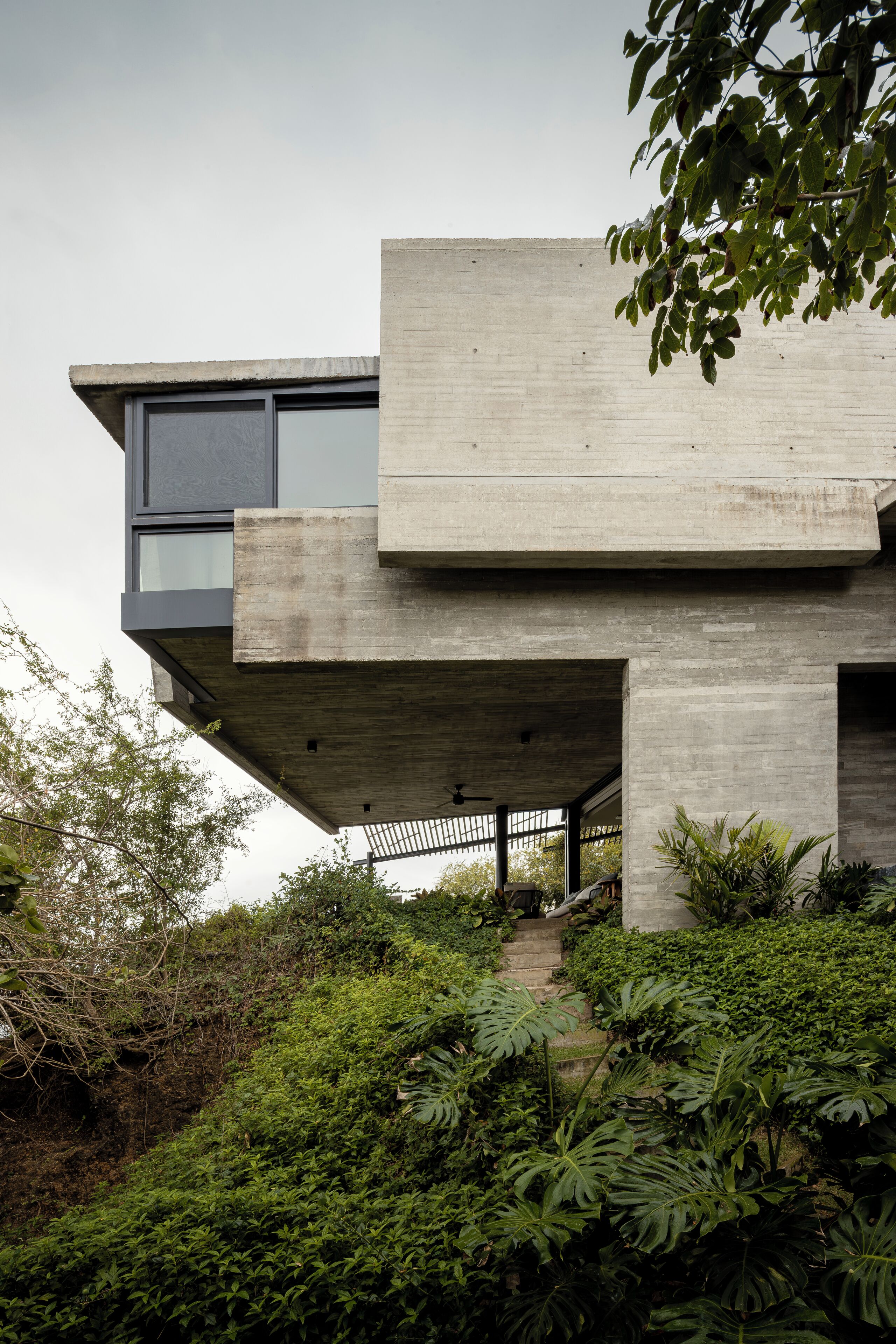 A modern concrete building with a flat roof, large windows, and a staircase leading to an upper level.