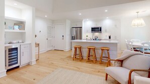 Una cocina moderna con gabinetes blancos, un refrigerador de acero inoxidable y un microondas. Hay tres taburetes de madera en la isla de la cocina.