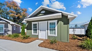 Een gelijkvloers huis met een groene gevel, witte details en een veranda.