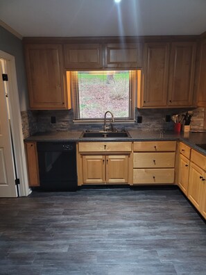 A kitchen with wooden cabinets, a black dishwasher, a granite countertop, and a window with blinds. - 2. Beautiful lakeview home in Guntersville (Guntersville)