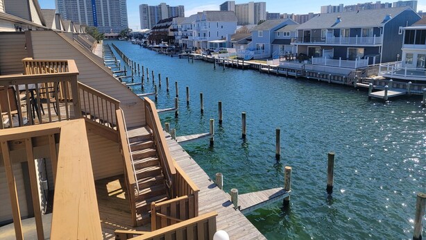 A waterfront property with a wooden deck, a dock extending into the water, and a row of houses along the water's edge.